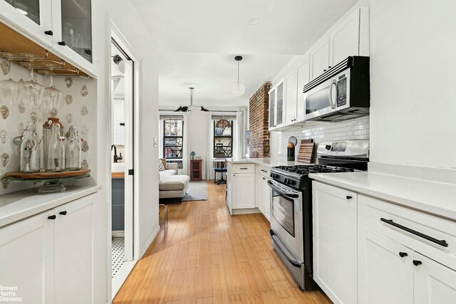 kitchen featuring light wood-type flooring, appliances with stainless steel finishes, white cabinets, and decorative light fixtures