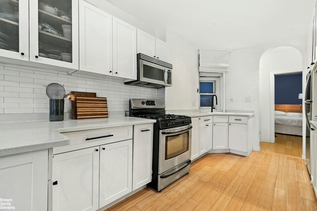 kitchen featuring white cabinetry, stainless steel appliances, sink, backsplash, and light wood-type flooring