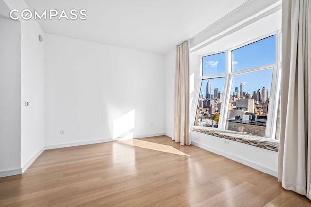 empty room featuring a city view, wood finished floors, and baseboards