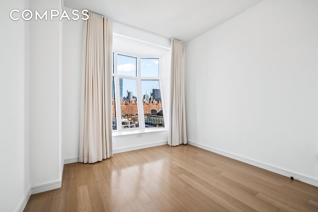 empty room featuring a healthy amount of sunlight, baseboards, a city view, and wood finished floors