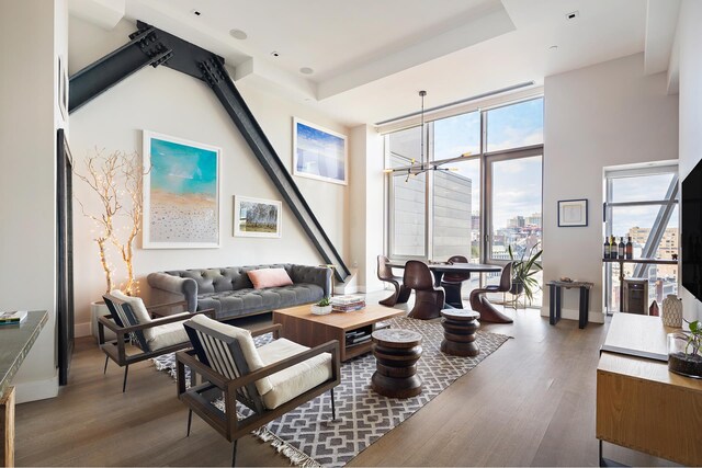 living area with an inviting chandelier, expansive windows, a raised ceiling, and wood finished floors