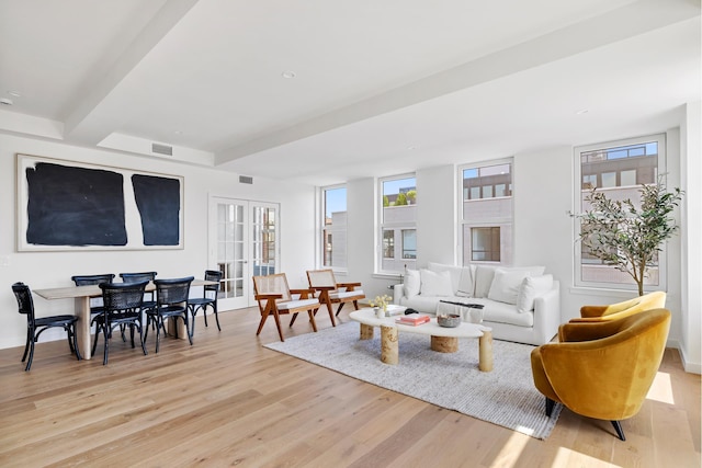 living room featuring visible vents, beam ceiling, plenty of natural light, and light wood-style flooring