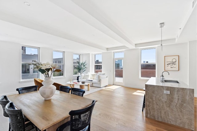 dining area with a healthy amount of sunlight, beamed ceiling, sink, and light hardwood / wood-style floors