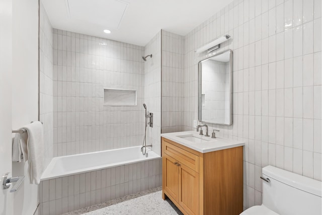 bathroom featuring toilet, tiled shower / bath combo, tile walls, vanity, and speckled floor