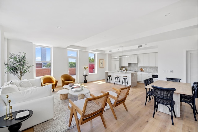 living room with light wood finished floors, visible vents, baseboards, recessed lighting, and a raised ceiling