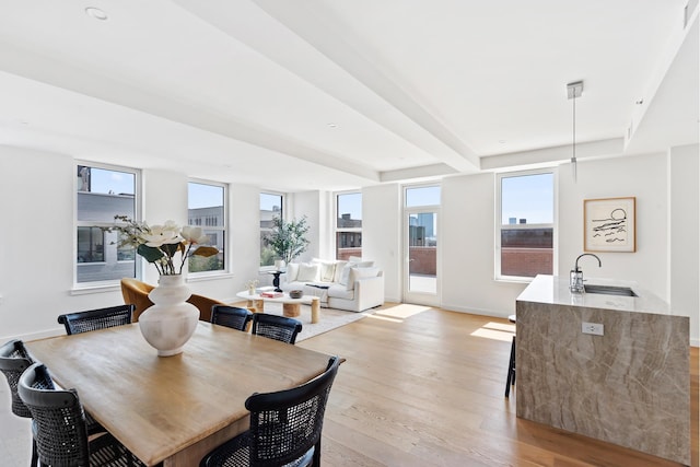 dining room with light wood-style flooring, baseboards, and beamed ceiling