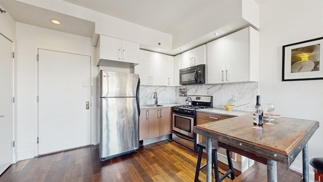 kitchen with appliances with stainless steel finishes, tasteful backsplash, dark hardwood / wood-style flooring, white cabinets, and sink