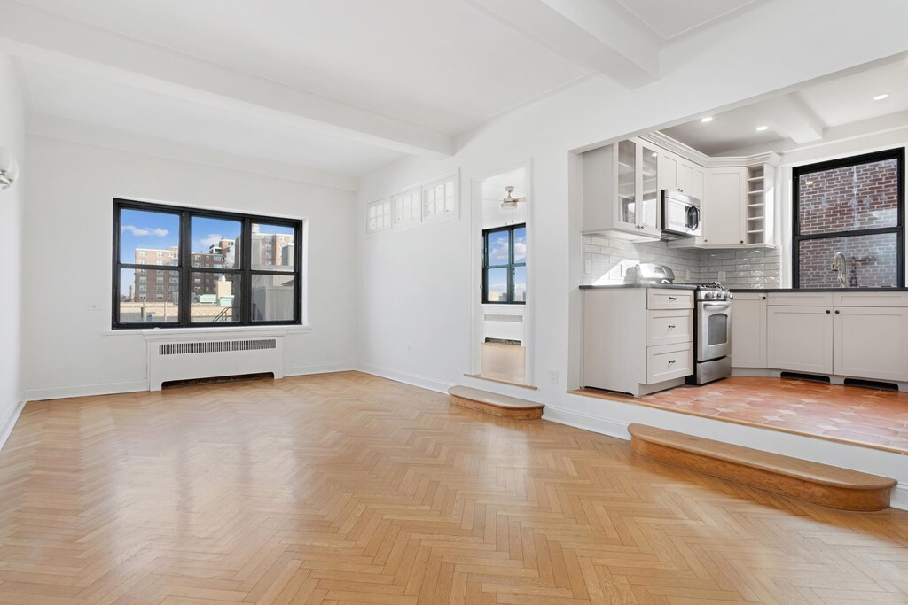 unfurnished living room featuring beam ceiling, radiator heating unit, baseboards, and a sink