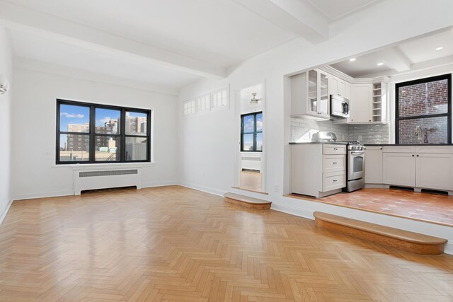 unfurnished living room featuring beam ceiling, radiator heating unit, baseboards, and a sink