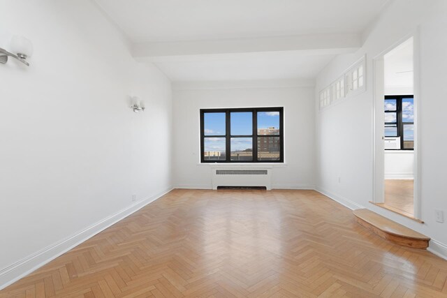 interior space with light parquet flooring, beamed ceiling, and radiator heating unit