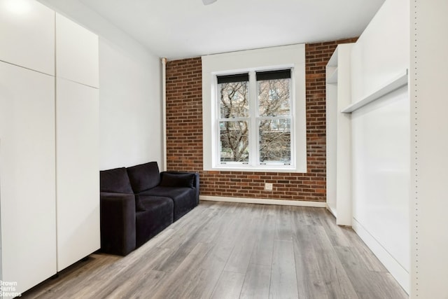 unfurnished room featuring brick wall and light hardwood / wood-style flooring