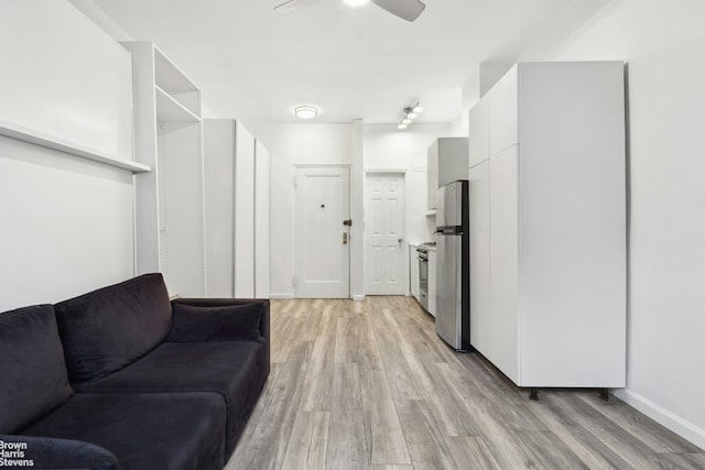living area with light wood-style flooring, a ceiling fan, and baseboards