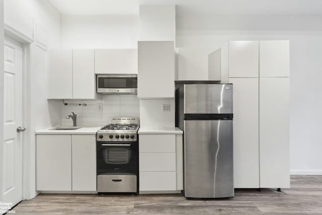 kitchen featuring light countertops, backsplash, white cabinetry, stainless steel appliances, and a sink