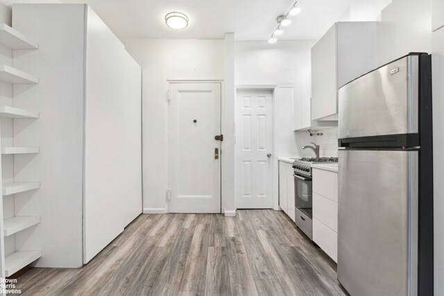 kitchen with backsplash, light wood-type flooring, appliances with stainless steel finishes, and white cabinetry