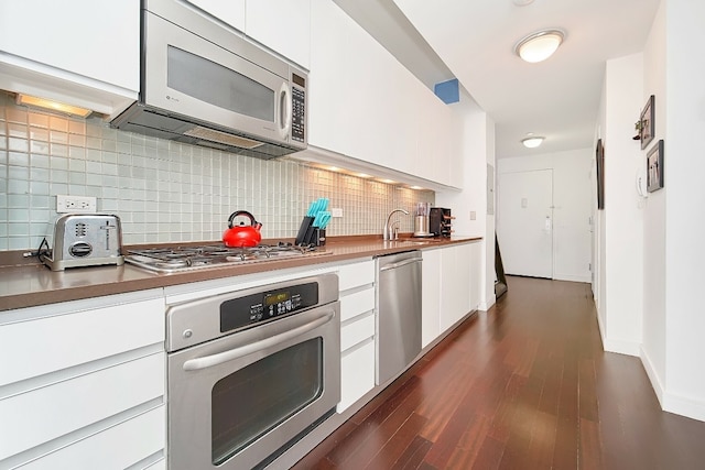 kitchen with tasteful backsplash, white cabinets, appliances with stainless steel finishes, and dark hardwood / wood-style flooring