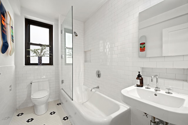 full bath with tile walls, toilet, tile patterned floors,  shower combination, and a sink