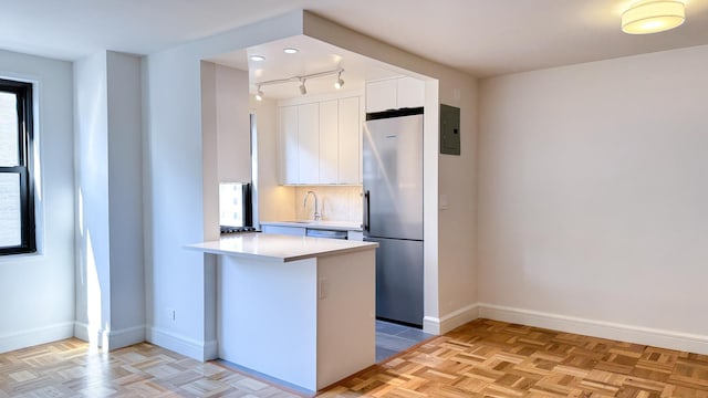 kitchen with decorative backsplash, white cabinets, baseboards, and freestanding refrigerator