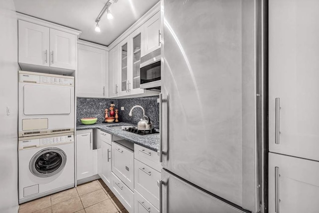 kitchen featuring light tile patterned flooring, white cabinetry, stacked washing maching and dryer, appliances with stainless steel finishes, and light stone counters