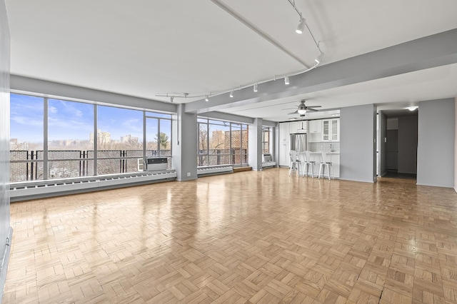 unfurnished living room with ceiling fan, rail lighting, baseboard heating, and a baseboard radiator