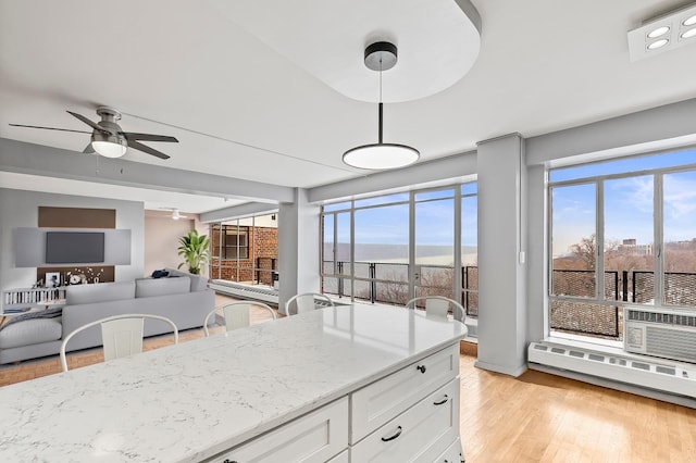 kitchen with light wood-type flooring, a ceiling fan, light stone counters, a baseboard heating unit, and white cabinets