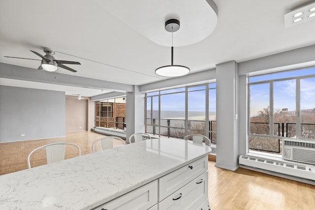 kitchen with ceiling fan, light stone countertops, baseboard heating, light wood-style floors, and white cabinetry