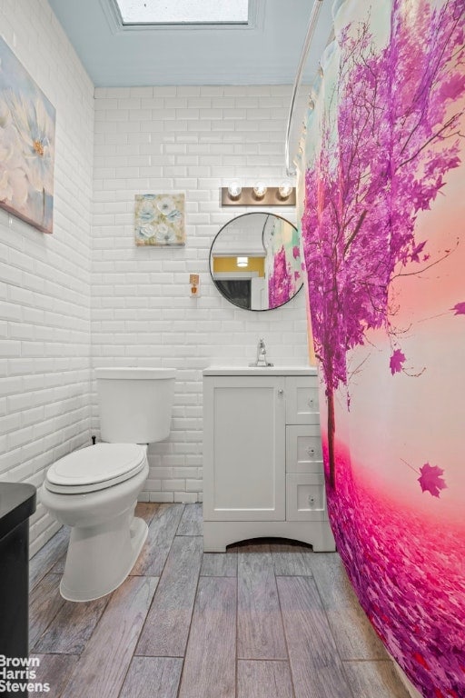 bathroom featuring toilet, brick wall, and vanity