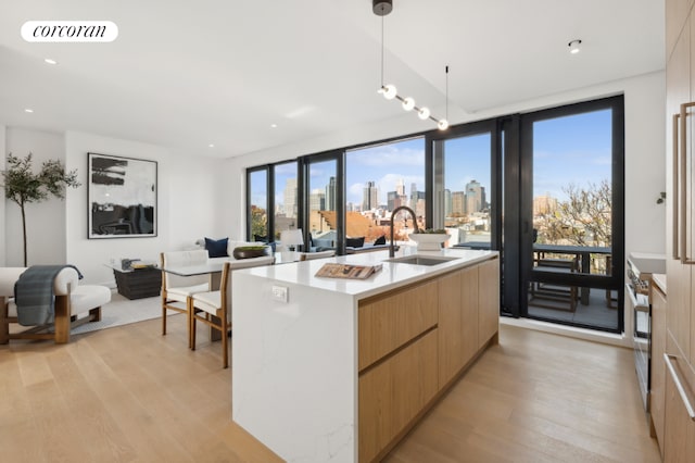 kitchen with an island with sink, sink, light wood-type flooring, and decorative light fixtures