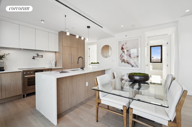 kitchen with white cabinets, sink, hanging light fixtures, high end stainless steel range oven, and a center island with sink