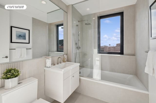 full bath featuring toilet, shower / bath combination with glass door, vanity, visible vents, and tile walls