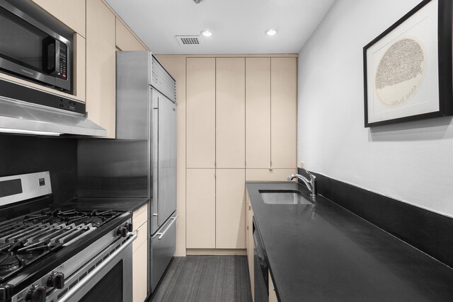 kitchen featuring stainless steel gas range oven, sink, dark hardwood / wood-style flooring, and cream cabinetry