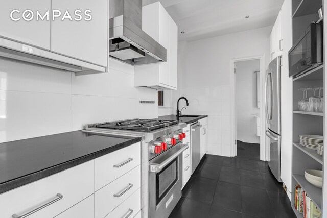 kitchen featuring white cabinetry, appliances with stainless steel finishes, tile walls, wall chimney exhaust hood, and sink