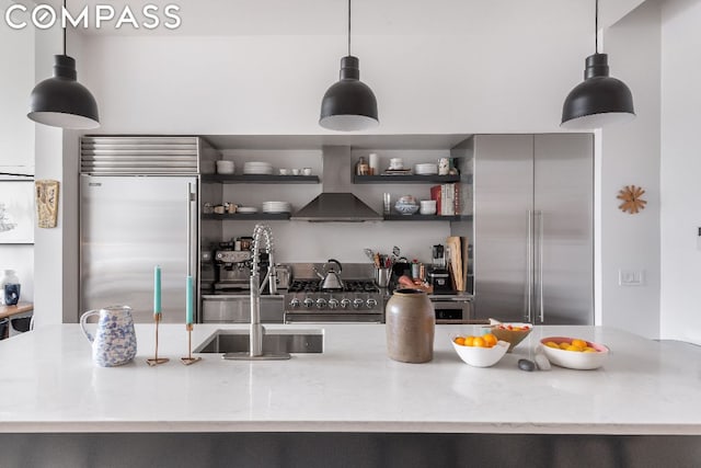 kitchen with hanging light fixtures, wall chimney exhaust hood, sink, and high quality appliances