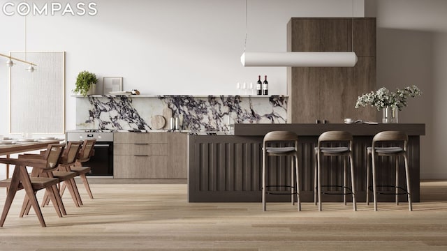 kitchen with decorative light fixtures, oven, a breakfast bar area, and light wood-type flooring