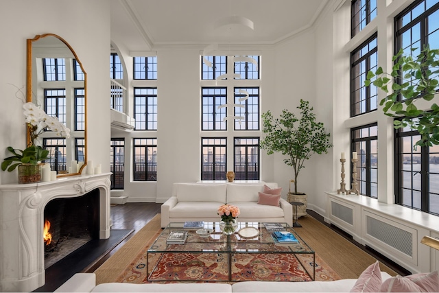 living area with wood finished floors, a towering ceiling, baseboards, a lit fireplace, and crown molding