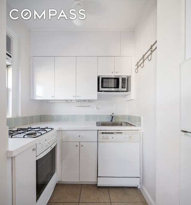 kitchen featuring light tile patterned floors, white appliances, a sink, white cabinets, and light countertops