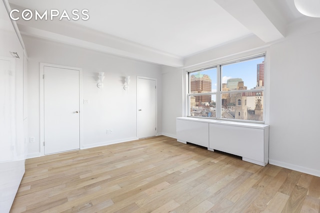 unfurnished room featuring baseboards, a city view, and light wood-style floors