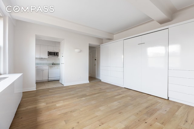 unfurnished bedroom with a closet, light wood-style floors, ensuite bath, beamed ceiling, and baseboards