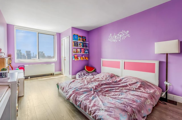 bedroom with baseboards, radiator heating unit, and wood finished floors