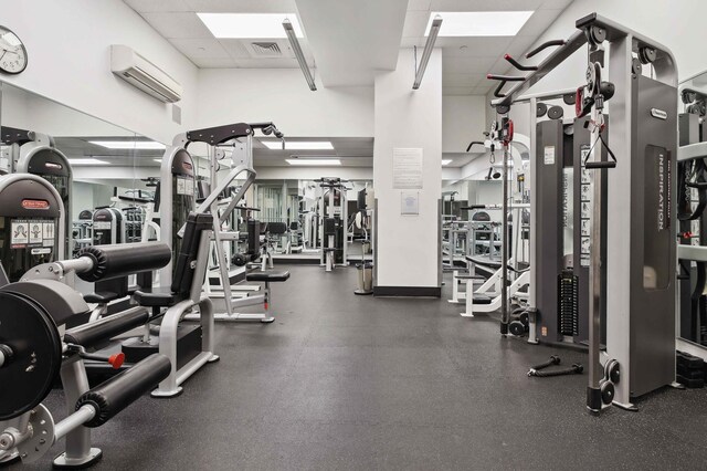 gym featuring a paneled ceiling, visible vents, and an AC wall unit