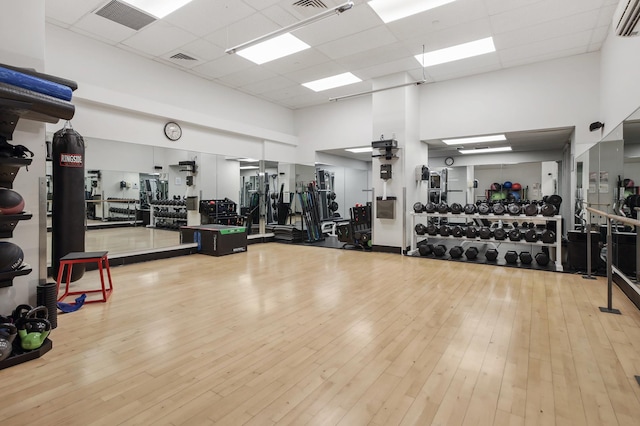 exercise room featuring a paneled ceiling, a high ceiling, visible vents, and hardwood / wood-style floors