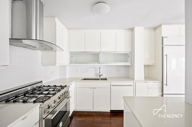 kitchen with tasteful backsplash, wall chimney range hood, built in fridge, stainless steel gas range, and a sink