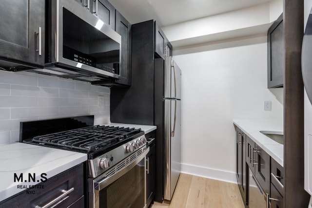 kitchen with backsplash, stainless steel appliances, light stone countertops, and light wood-type flooring