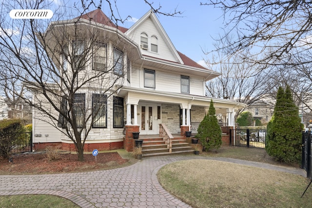 victorian house featuring a porch, a gate, fence, and stone siding