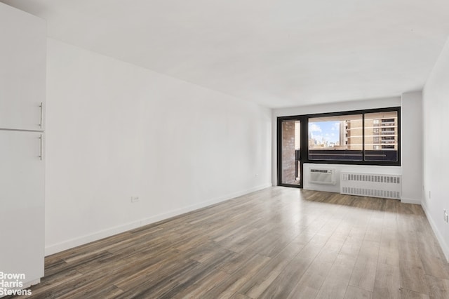 unfurnished living room featuring radiator, a wall mounted air conditioner, and hardwood / wood-style flooring