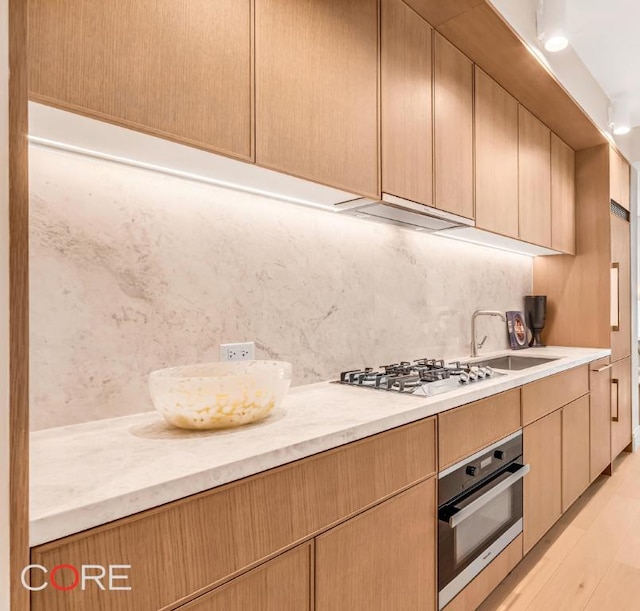 kitchen featuring stainless steel appliances, decorative backsplash, light wood-type flooring, light brown cabinetry, and sink