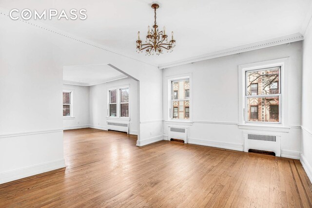 unfurnished dining area with radiator, wood finished floors, and a chandelier