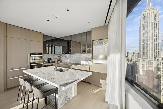 kitchen with sink, light hardwood / wood-style flooring, a kitchen bar, decorative backsplash, and stainless steel double oven