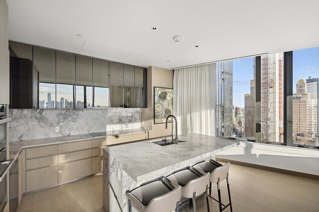 kitchen featuring sink, a breakfast bar, a center island with sink, decorative backsplash, and light wood-type flooring