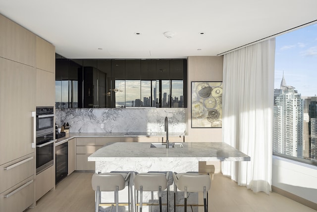 kitchen featuring sink, light hardwood / wood-style flooring, a breakfast bar, backsplash, and a center island with sink