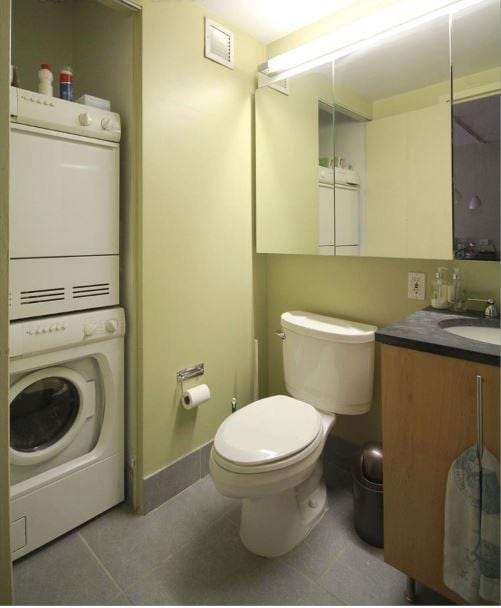 bathroom with toilet, stacked washer / dryer, tile patterned flooring, and vanity